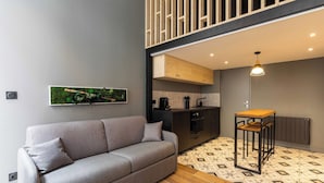 Ein modernes Wohnzimmer mit einem grauen Sofa, einem kleinen Holztisch und einer Küchenzeile mit Schränken und einer Heizung.