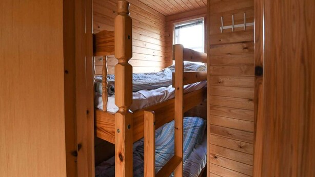 Quarto de cabana de madeira com beliches, uma janela e teto de madeira.