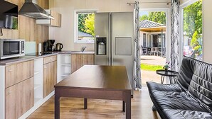 Une cuisine moderne avec des armoires en bois, un four à micro-ondes en acier inoxydable et un four encastré. On y trouve une table à manger et un canapé en cuir noir dans l’espace salon.
