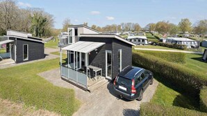 A modern RV park with compact, dark-colored cabins, a covered outdoor seating area, and a car parked in front. - 4 Person Holiday Park Home in Krusa (Krusaa)