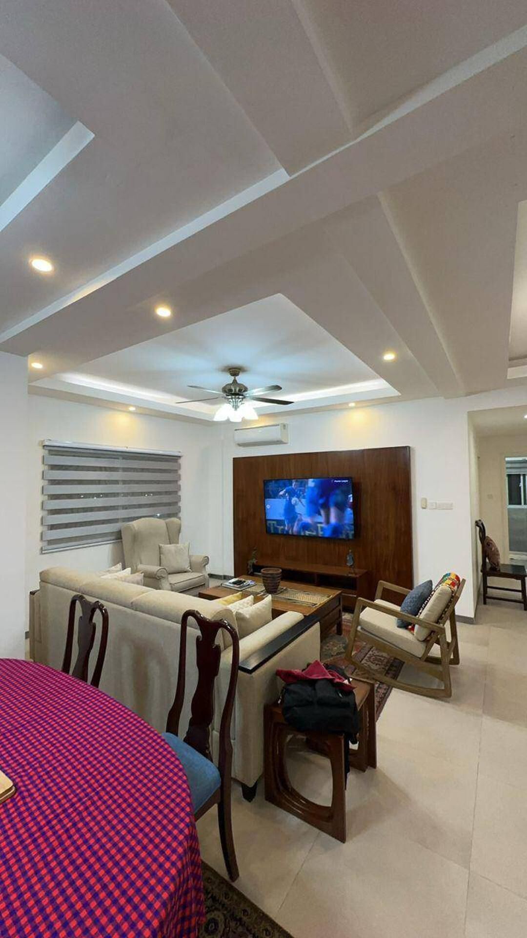 A living room with a sofa, chairs, a coffee table, a TV, and a ceiling fan.