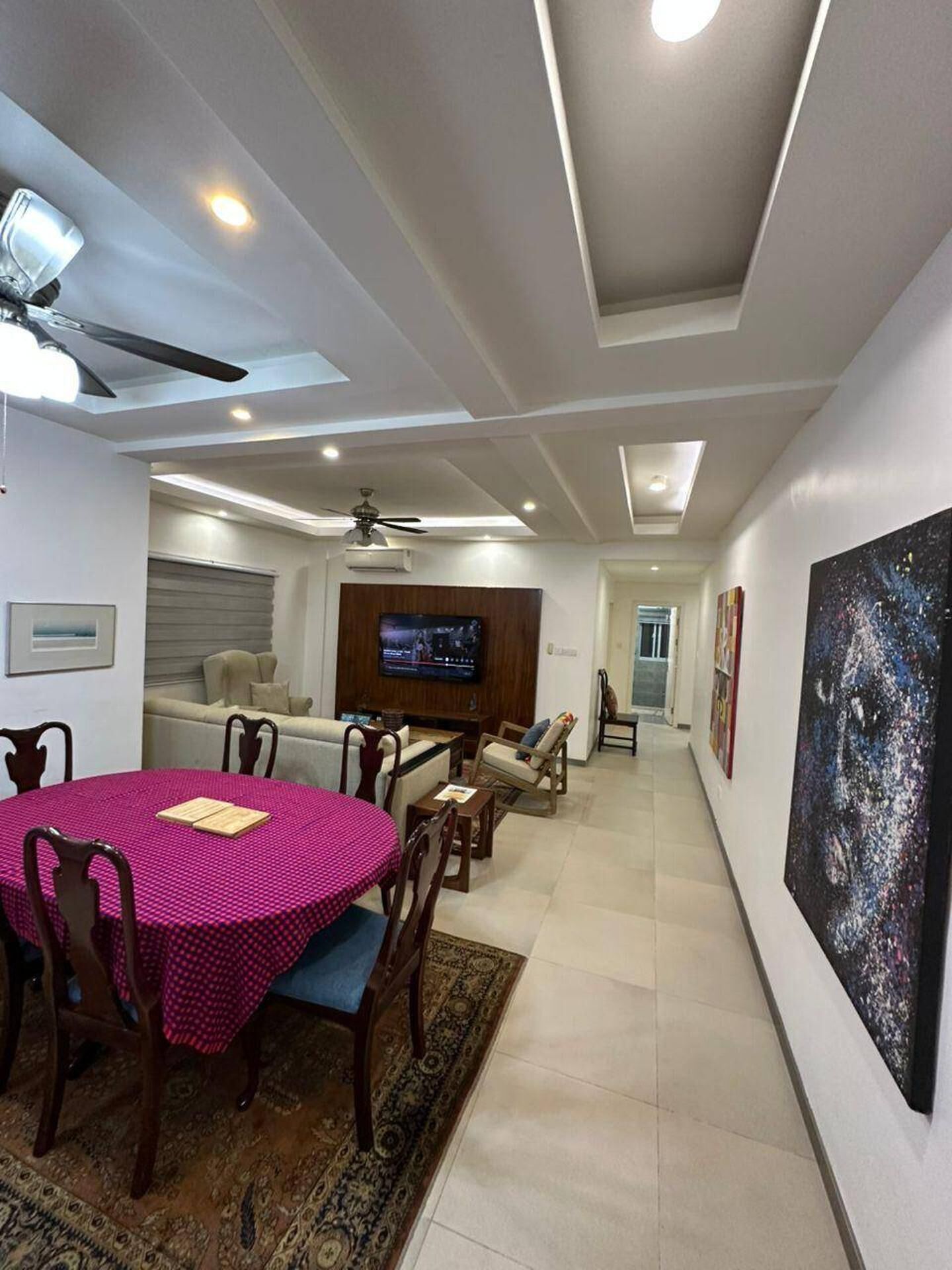 A modern living room with a dining area, a TV mounted on the wall, and a large abstract painting.