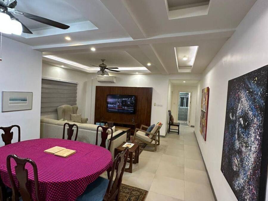 A modern living room with a dining area, a TV mounted on the wall, and a large abstract painting.