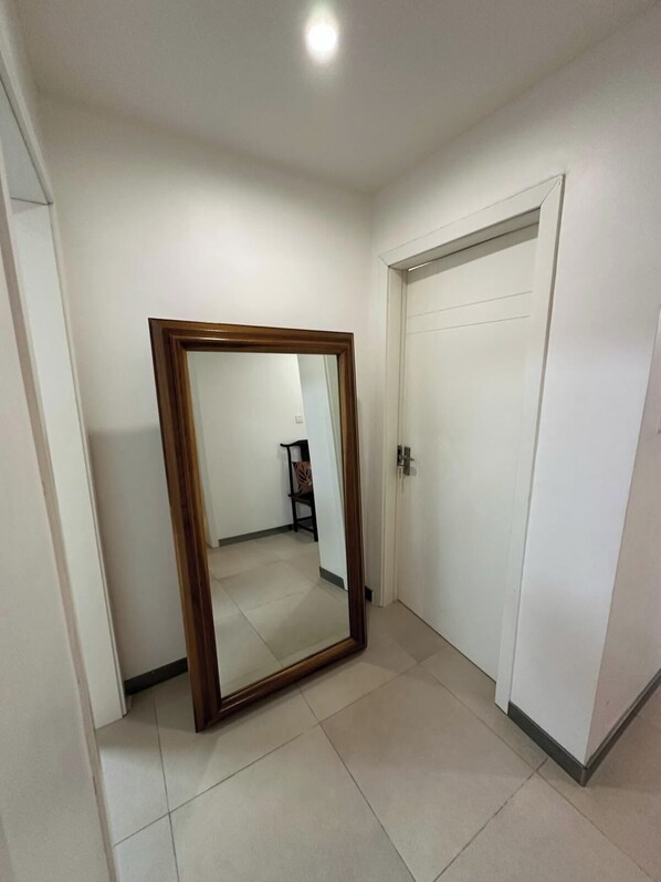 A hallway with a large mirror, a white door, and a tiled floor.