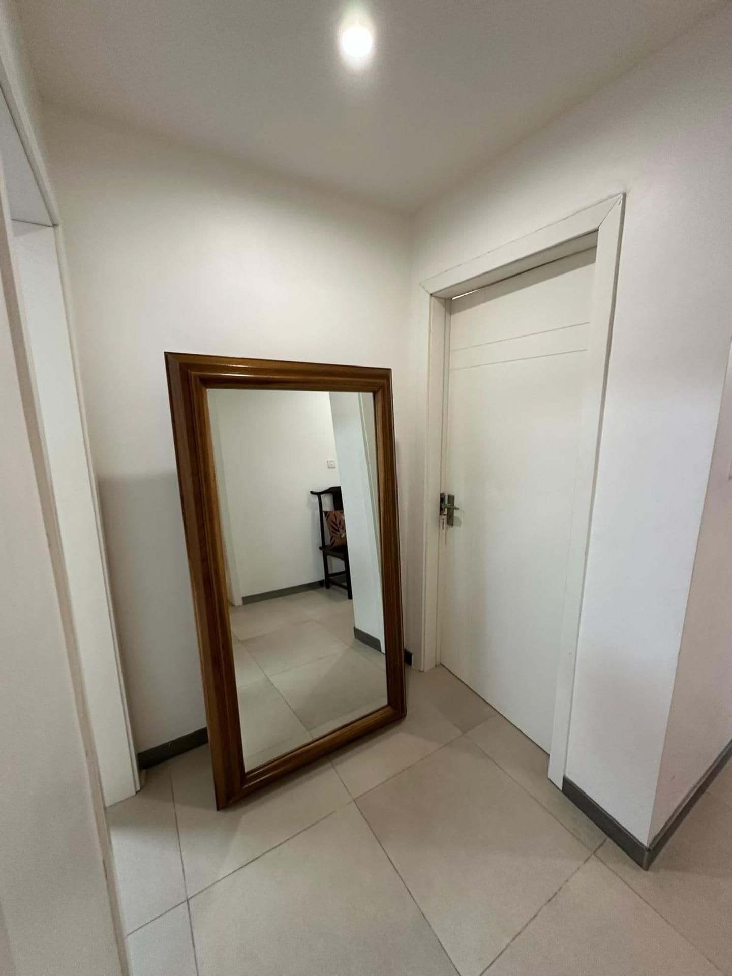 Un corridoio con uno specchio grande, una porta chiusa e un pavimento piastrellato.