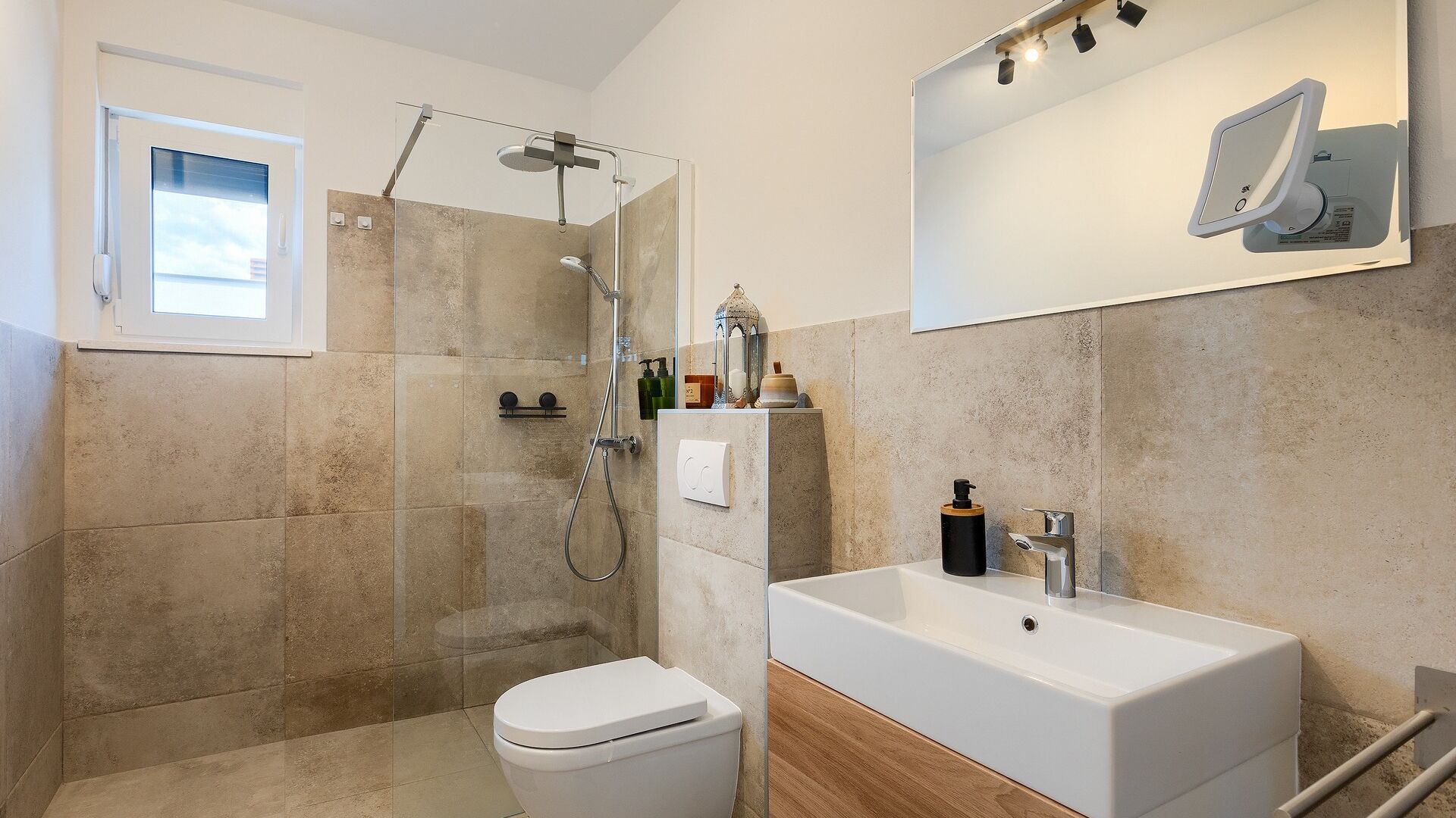 Un bany modern amb dutxa tancada per vidre, un vàter blanc, un lavabo amb armari de fusta i un mirall amb il·luminació.