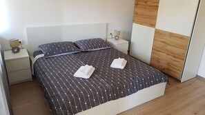 Een bed met een beddengoed met geometrisch patroon, twee kussens, een nachtkastje met een lamp en een wandpaneel van hout.