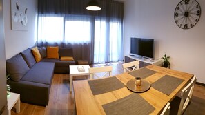 Een moderne woonkamer met een bank, een eettafel, een televisie en een klok aan de muur.