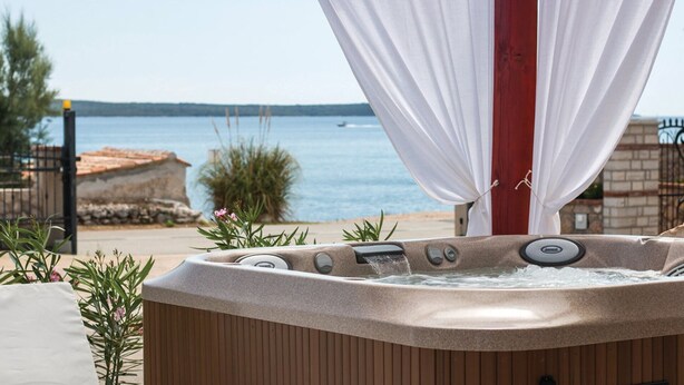 Un bain à remous avec vue sur la mer, entouré de plantes et d’un rideau blanc.