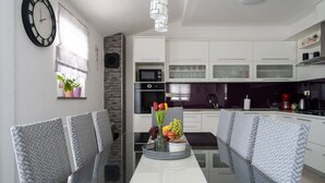 A modern kitchen with white cabinets, a black countertop, and a dining area with a glass table and patterned chairs. - Villa Klarita - Makarska by Villas Guide (Drum)