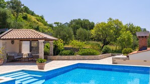 A swimming pool with a tiled deck, a covered seating area with a table and chairs, and a stone wall. - Villa None Kate by Villas Guide (Dubrovnik)