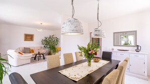 A modern living room with a dining area, featuring a dark wooden table, beige chairs, and a large potted plant. - Villa None Kate by Villas Guide (Dubrovnik)