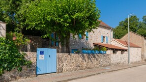 A stone building with a blue door, a tree in front, and a clear blue sky.