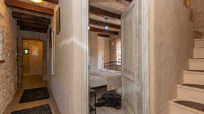 A narrow hallway with a wooden ceiling, a bed with a white headboard, a small table, and a dog lying on the floor.