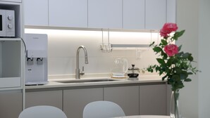 Une cuisine moderne équipée d’une machine à café intégrée, d’un évier et d’une cafetière en verre posée sur le plan de travail. Un vase rempli de fleurs est placé sur la table.