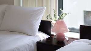Une chambre d’hôtel avec un lit, une table de chevet surmontée d’une lampe rose et une fenêtre avec des rideaux.