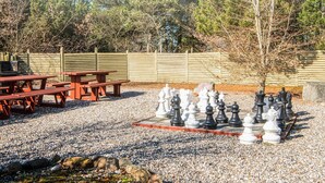 A chessboard set up on a gravel surface with picnic tables and a wooden fence in the background. - 4 Person Holiday Park Home in Pandrup (Pandrup)