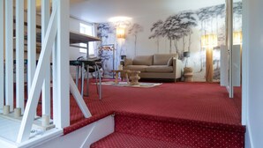 Un salon avec une moquette rouge, un canapé beige et un escalier recouvert d’une moquette rouge.