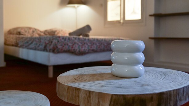 Une pièce avec un lit, une lampe et un vase blanc posé sur une table en bois.