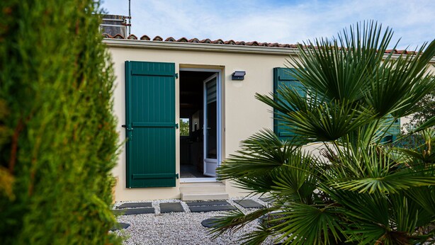 A building with a beige facade, green shutters, and a gravel pathway leading to the entrance. - Charming holiday home near Tanchet beach (Les Sables-d´Olonne)