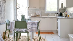 A modern kitchen with white cabinets, a dining table with chairs, and a window providing natural light. - Charming holiday home near Tanchet beach (Les Sables-d´Olonne)