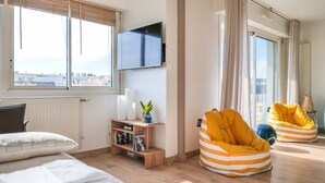 A modern living room with a large TV, bean bags, a bookshelf, and a view of the city. - Charming apartment in the Presidents' District (Les Sables-d´Olonne)