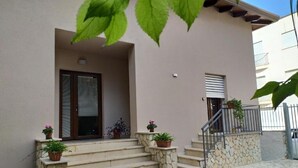 A building with a stone staircase leading to a door, potted plants on the steps, and a metal railing on the right.