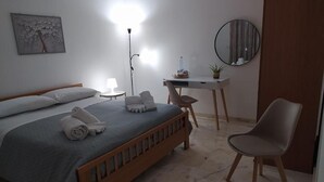 A bedroom with a bed, a desk, a chair, a lamp, a mirror, and a wall art piece.