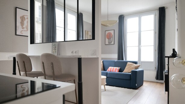 A modern living room with a blue sofa, a dining area with a white table, and a kitchen area with a refrigerator. - Apartment for 2, Ideal Location in Downtown Angers (Angers)