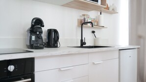 A modern kitchen with white cabinets, a black coffee maker, a kettle, and a dishwasher. - Apartment for 2, Ideal Location in Downtown Angers (Angers)