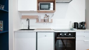Uma cozinha moderna com micro-ondas embutido, forno e máquina de lavar louça. Há prateleiras de madeira acima do balcão e uma cafeteira à direita.