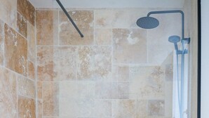 Et bruseområde med glasdør, beige fliser og et hvidt badekar.