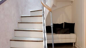 Una escalera con peldaños de madera y barandilla metálica que conduce a una habitación con un sofá blanco y piso de madera.