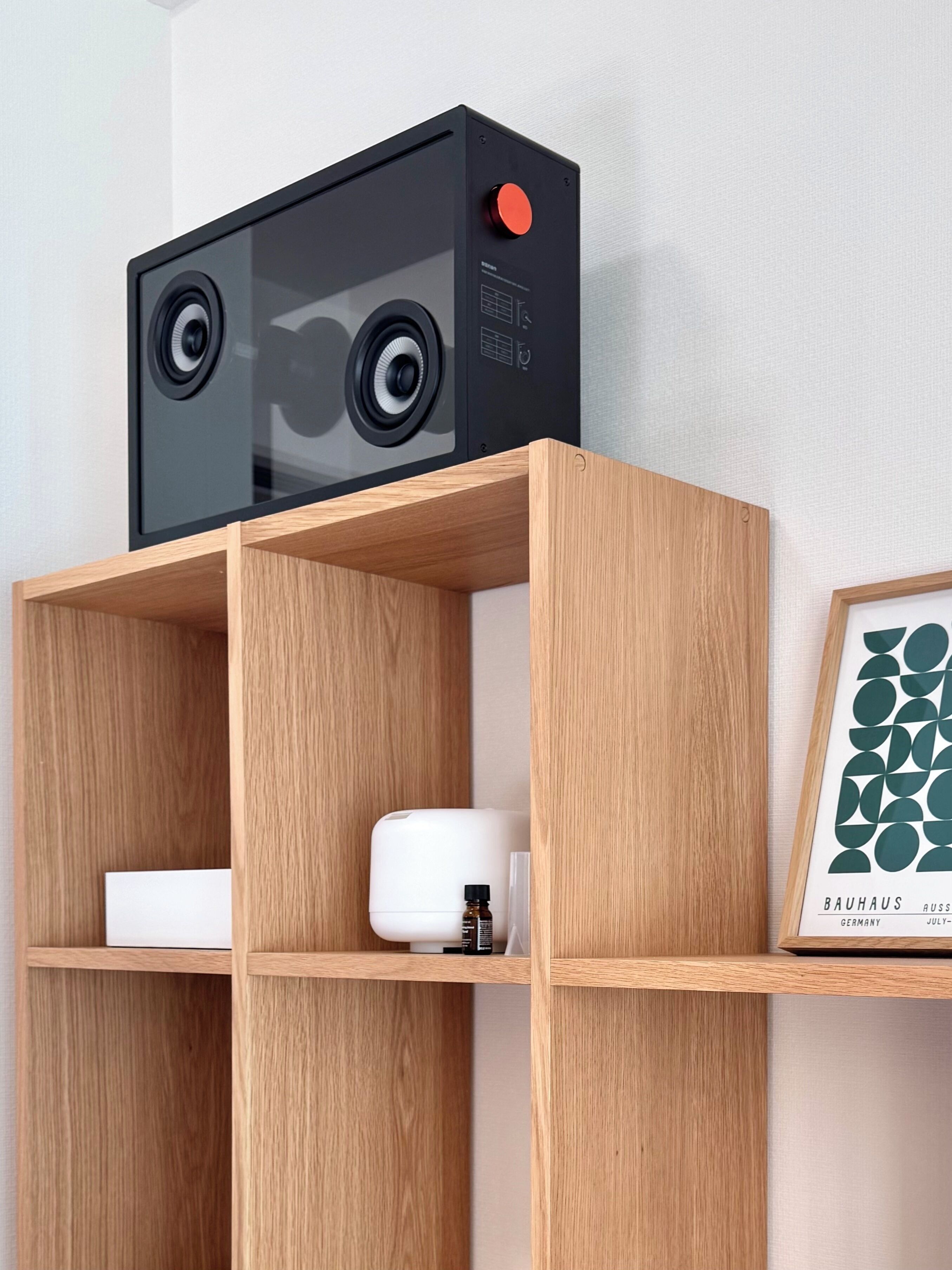 Une étagère en bois sur laquelle se trouvent un appareil électronique noir, un récipient blanc et un tableau encadré.