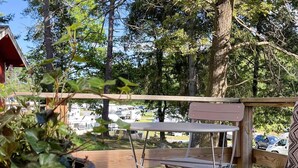 Une terrasse en bois avec une table et des chaises, entourée d’arbres, et en arrière-plan, on aperçoit des camping-cars.