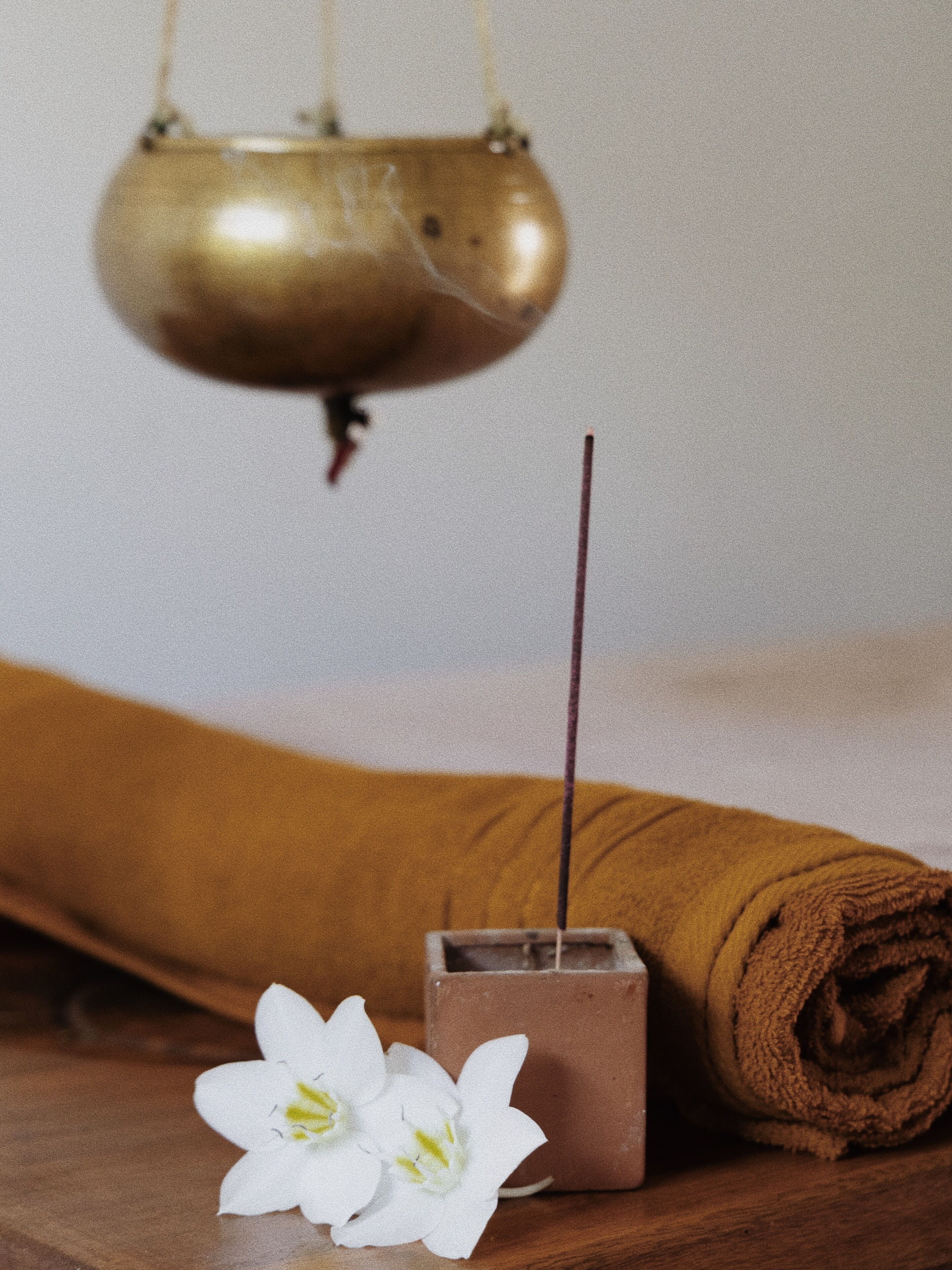 A wooden table with a rolled-up brown towel, a small metal container, and two white flowers.