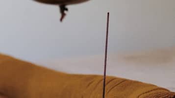 A wooden table with a rolled-up brown towel, a small metal container, and two white flowers.