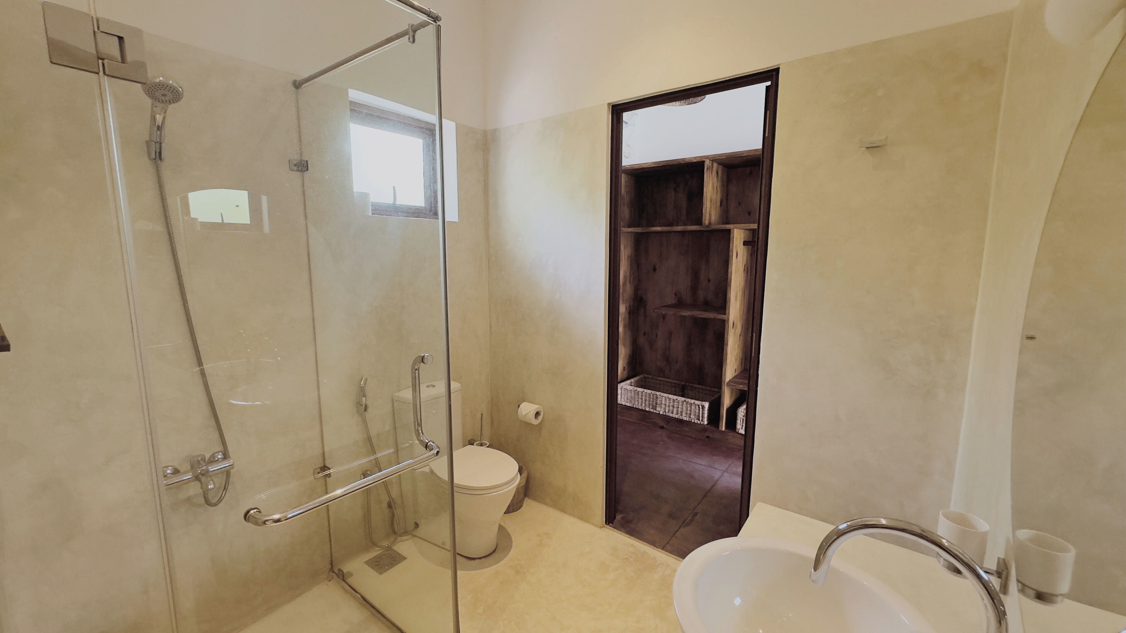 Un baño con ducha de vidrio, inodoro, lavamanos y estante de madera.