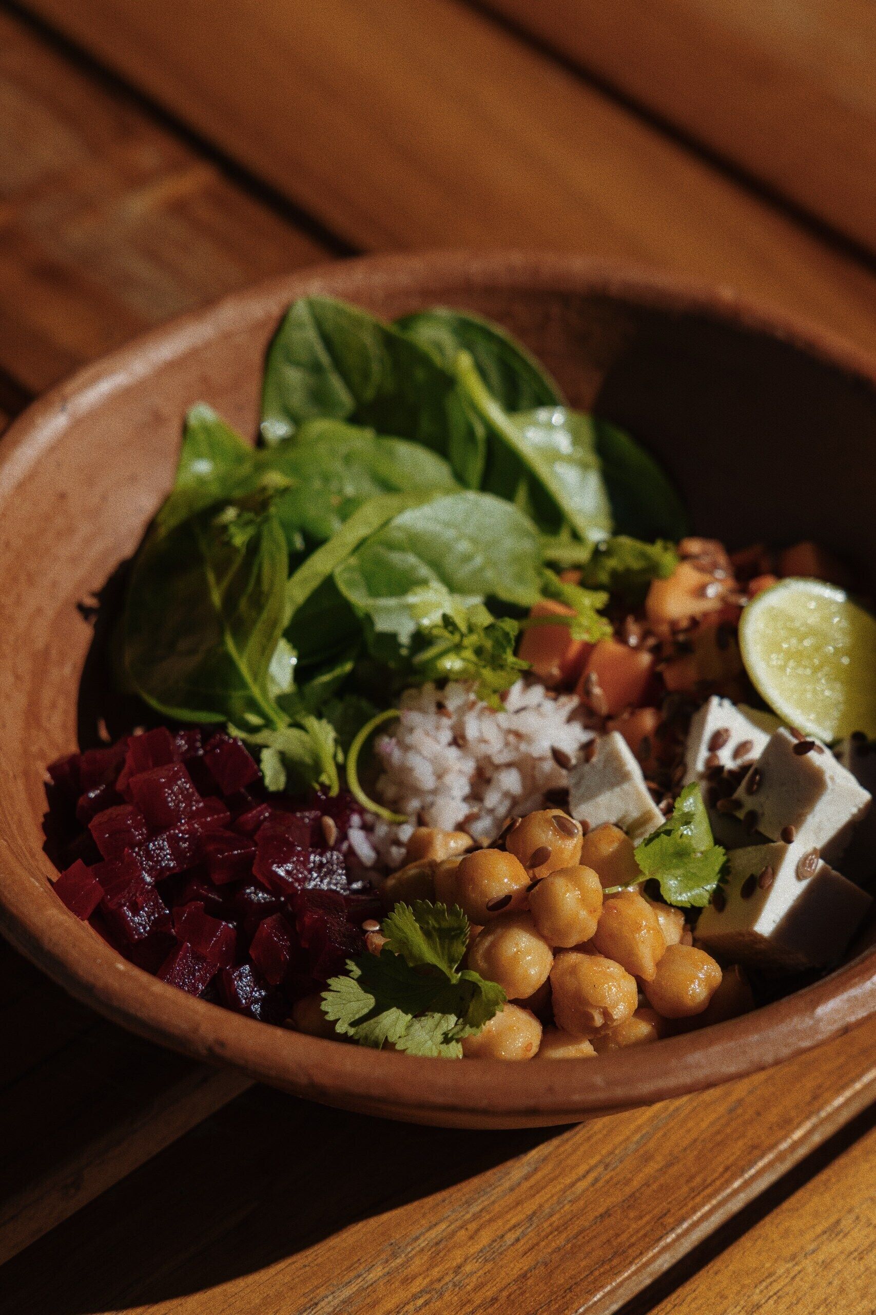 A wooden bowl filled with various ingredients including chickpeas, beets, and leafy greens.