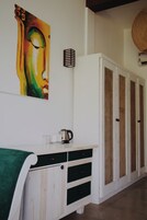 Una habitación con un armario blanco, una toalla verde, un cuadro y una cesta de mimbre.