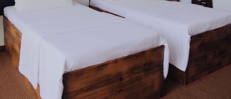 Two wooden beds with white linens in a room with dark wooden walls and a wooden ceiling beam.
