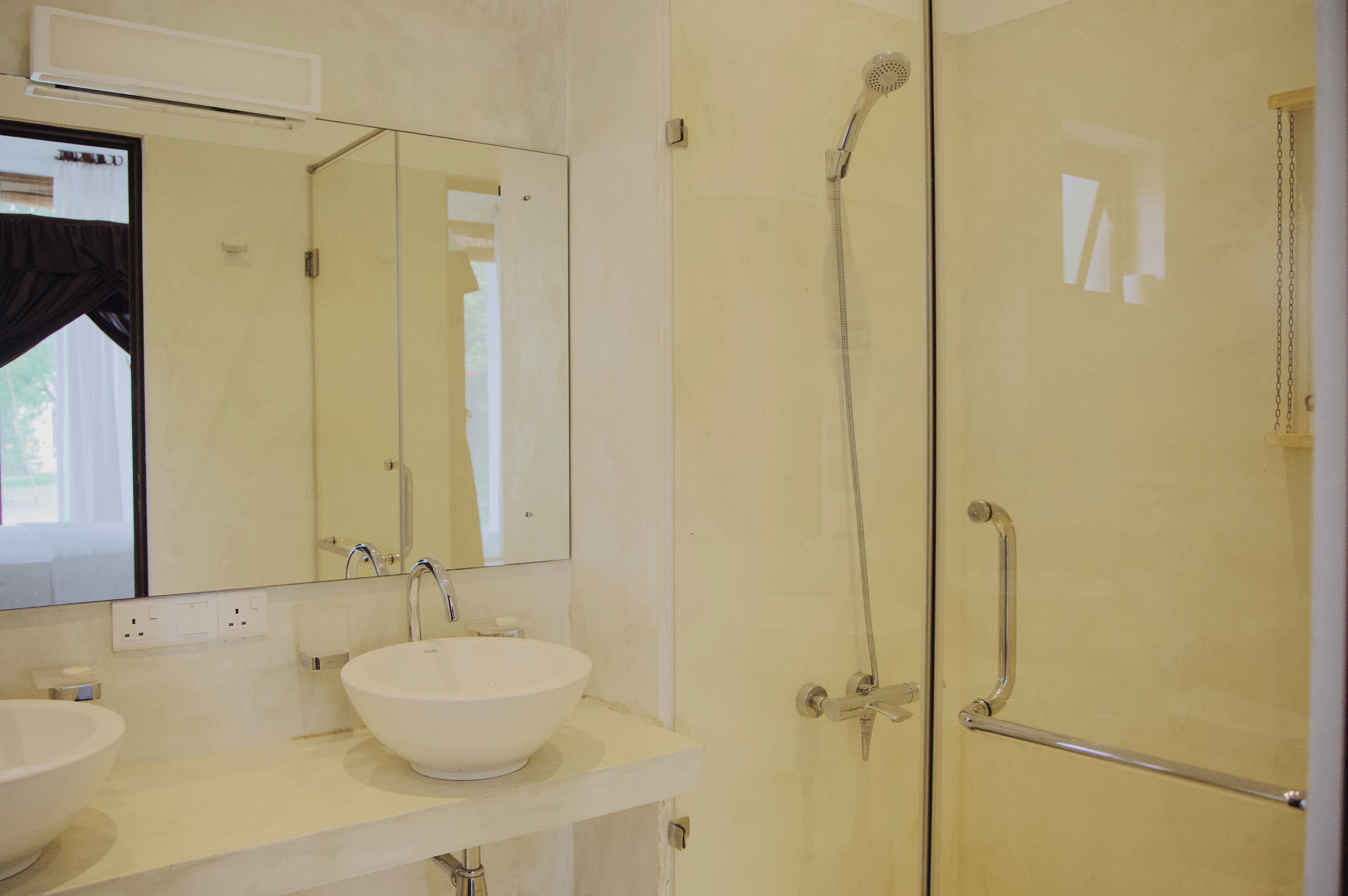 A modern bathroom with a large mirror, a white sink, and a shower with a handheld showerhead.