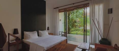 Un dormitorio con cama, escritorio, silla, ventilador de techo y vistas de un jardín a través de una puerta corredera.