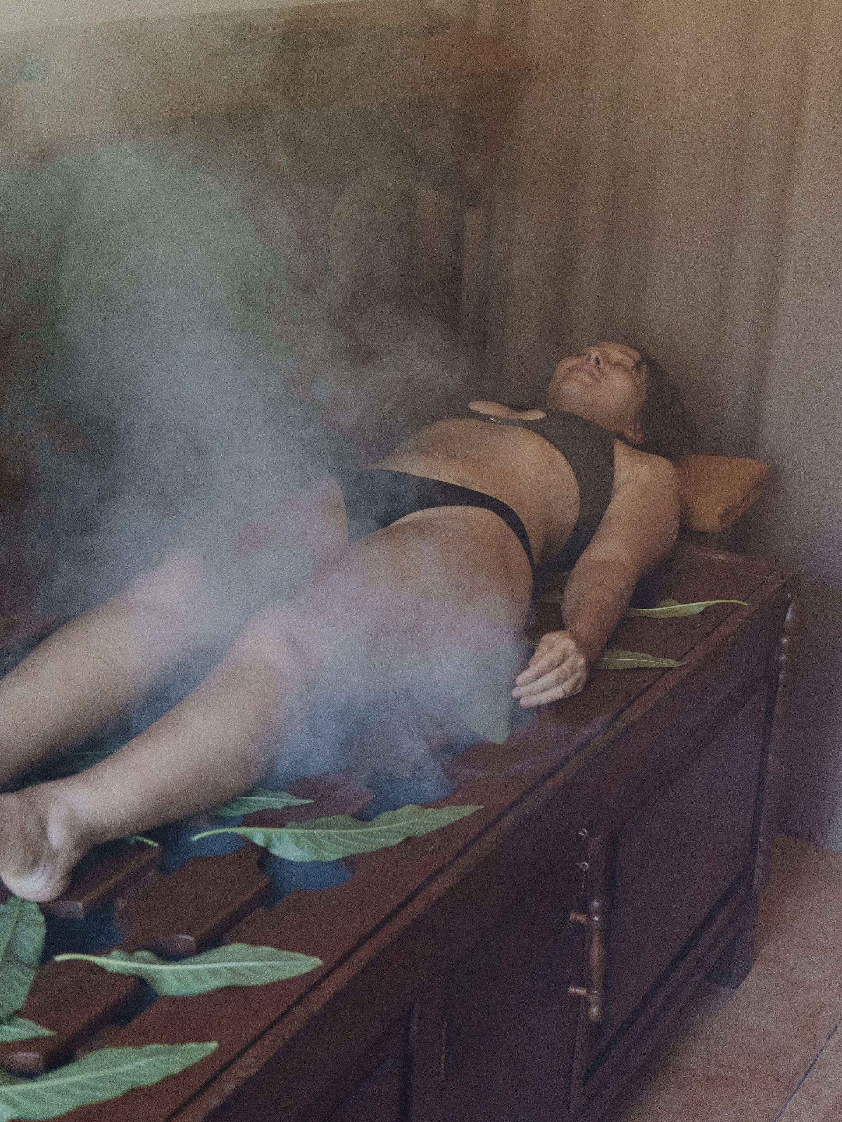 A person lying on a wooden bench with steam rising from it.