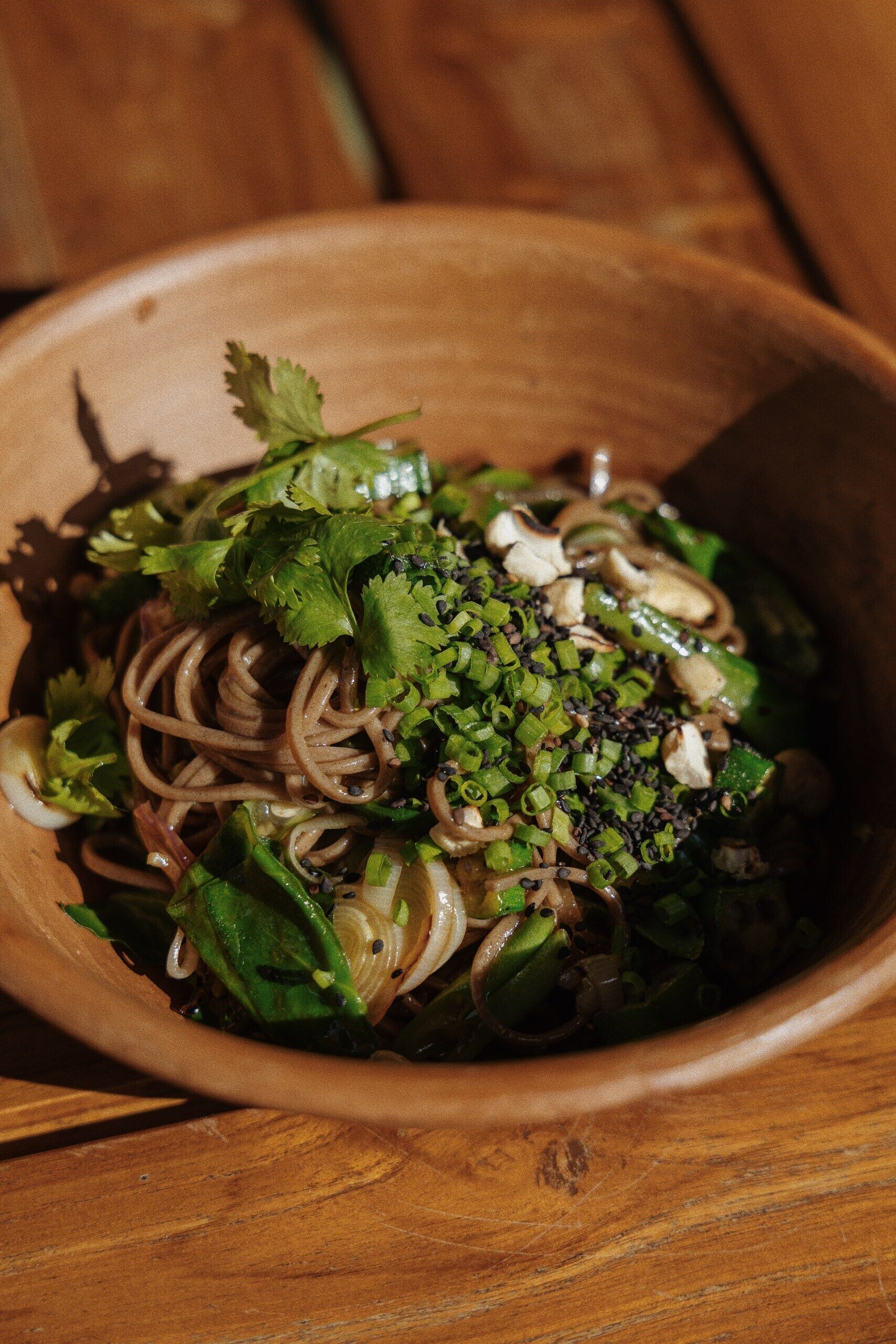 A wooden bowl filled with noodles, green onions, and cilantro.