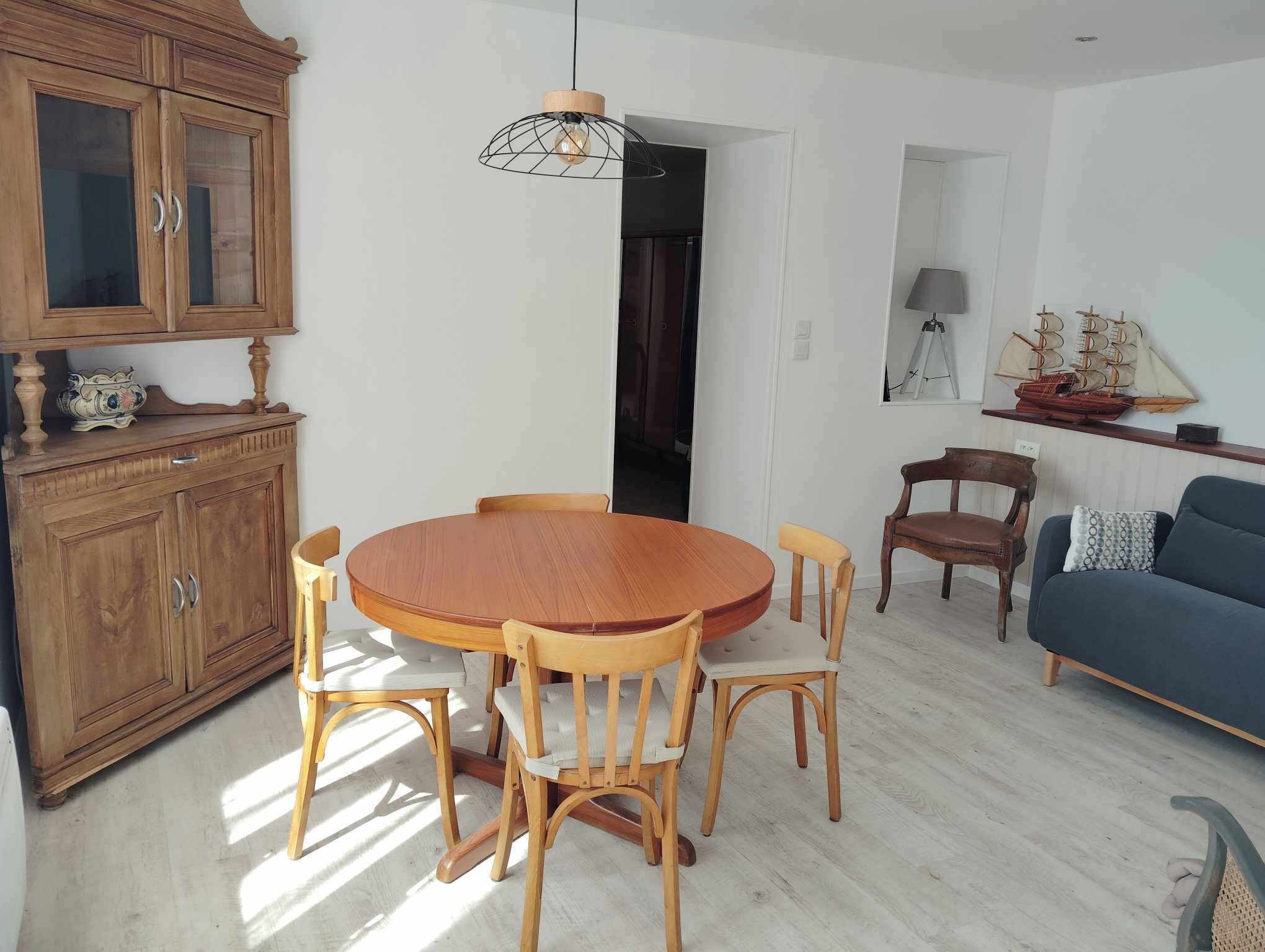 Un coin repas avec une table et des chaises en bois, un meuble avec des portes en verre et un luminaire suspendu.