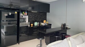 Cozinha moderna com armários pretos, bancada preta e forno embutido. Há três banquetas e um sofá branco na sala de estar.