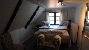 Een kleine, zwak verlichte kamer met een bed, twee stoelen, een radiator en een raam met gordijnen.