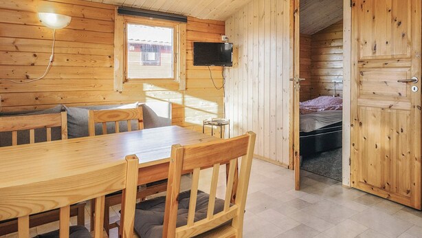 A wooden cabin interior with a dining table, chairs, a television, and a bed. - 6 Person Holiday Park Home in Gorlev (Gørlev)
