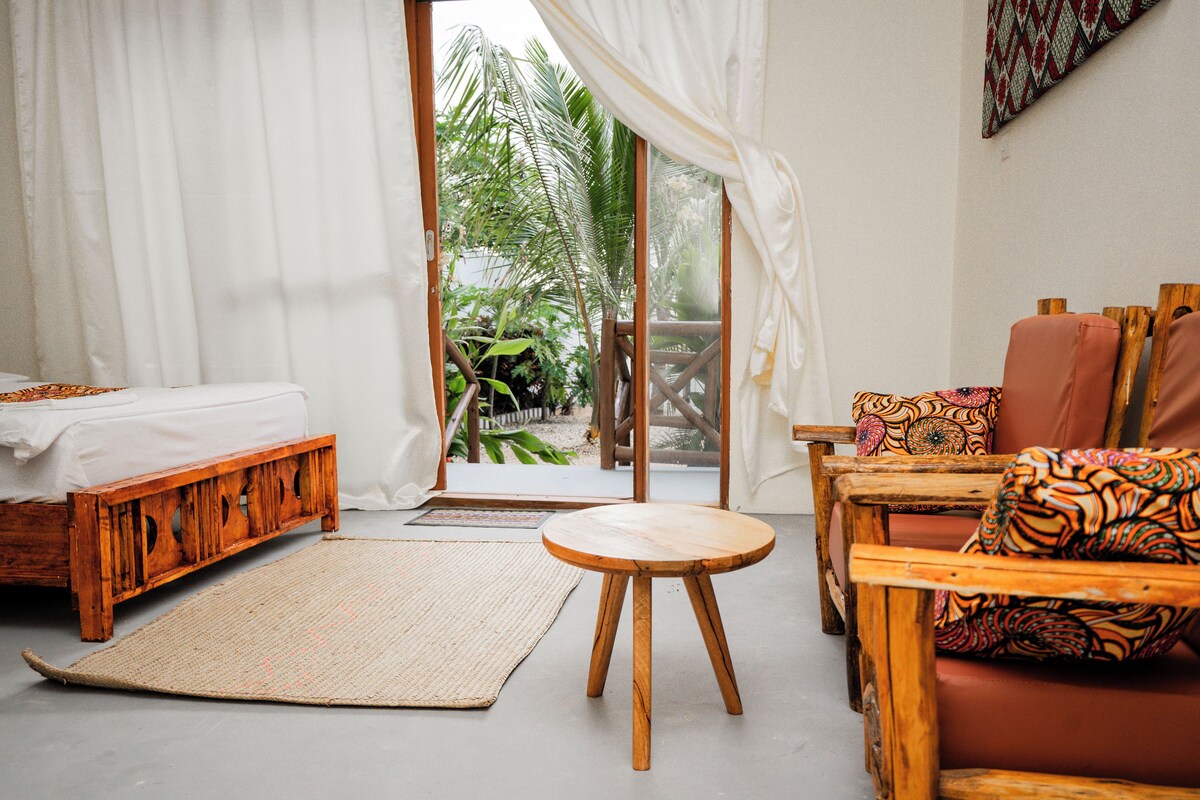A room with a bed, a wooden bench, a round wooden table, and a sofa with patterned cushions.
